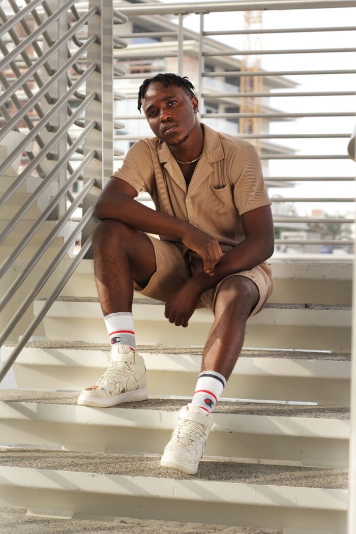 our-story African American man in fashionable attire sitting on a modern outdoor staircase in Dubai.
