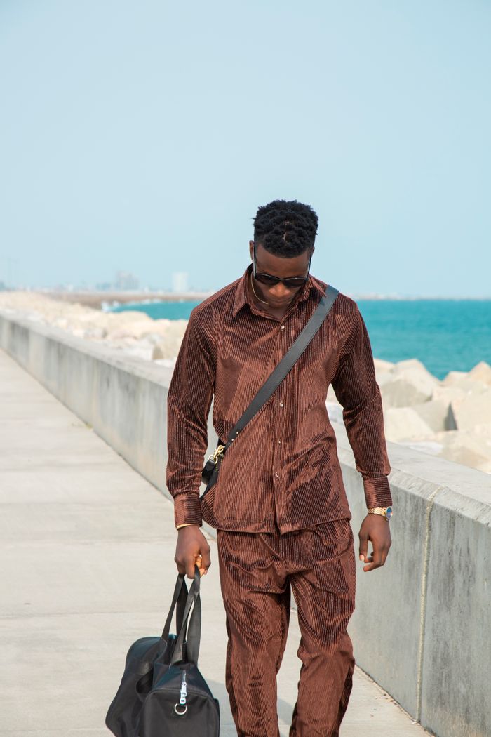 services-02 Man in brown suit walking along a seaside promenade carrying a leather bag.